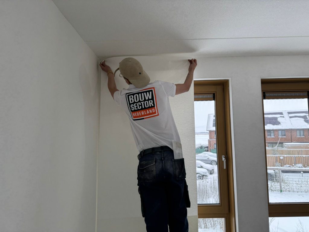Behanger van Bouwsector Nederland zet een baan renovlies tegen het plafond van een nieuwe kamer, buiten ligt sneeuw