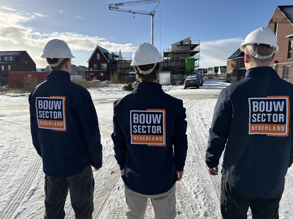 Drie vakmensen met witte bouwhelm kijken naar woningen in aanbouw